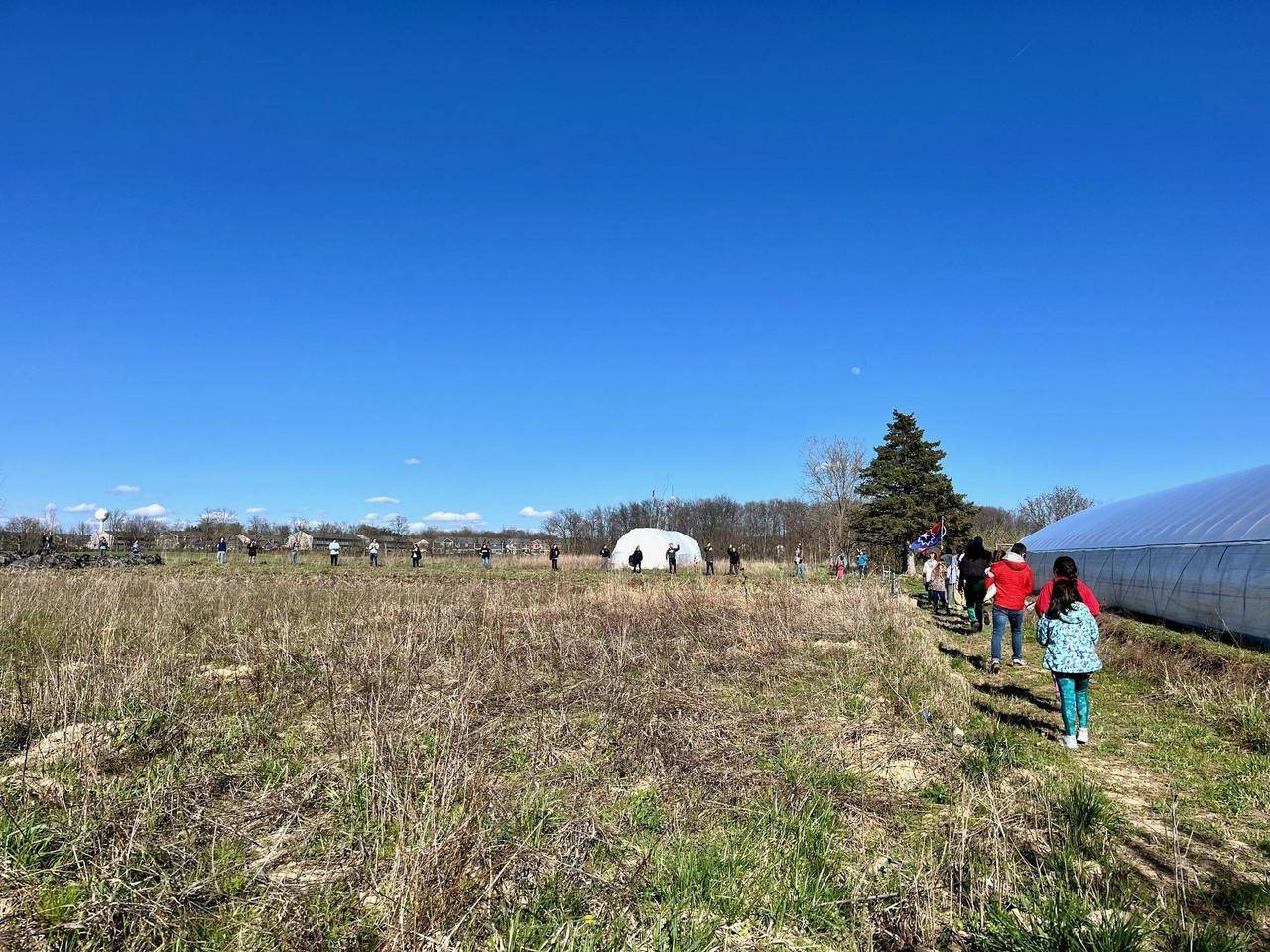 a line of people standing around the edge of a square meadow for a land blessing